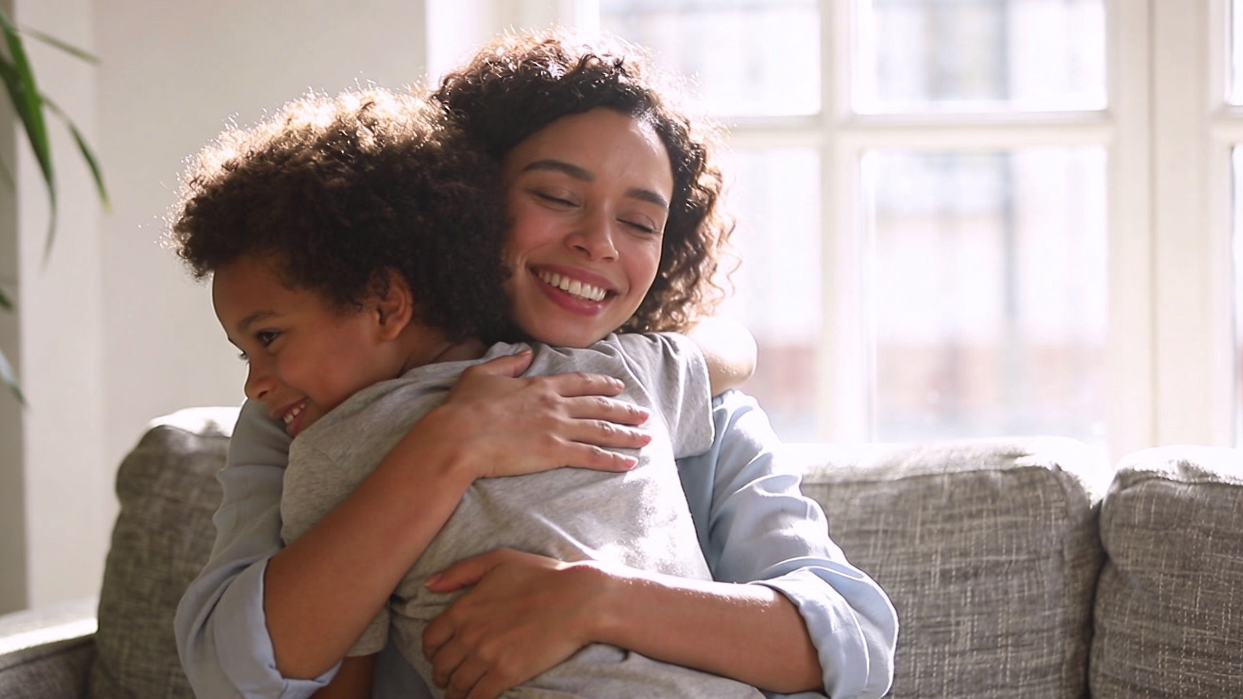 A loving mother warmly embraces her young curly-haired son at home, showing their deep bond and affection.